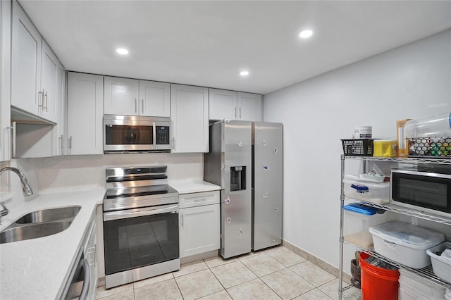 kitchen featuring decorative backsplash, stainless steel appliances, sink, light tile patterned floors, and white cabinetry