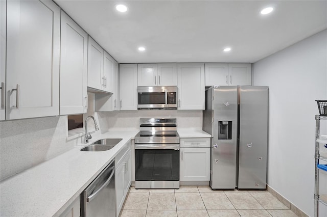 kitchen featuring sink, light stone countertops, light tile patterned floors, white cabinetry, and stainless steel appliances