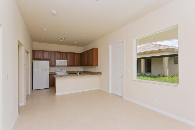 kitchen with kitchen peninsula, a wealth of natural light, light tile patterned flooring, and white appliances