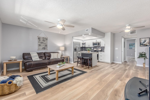 living room with a textured ceiling, light hardwood / wood-style flooring, and ceiling fan