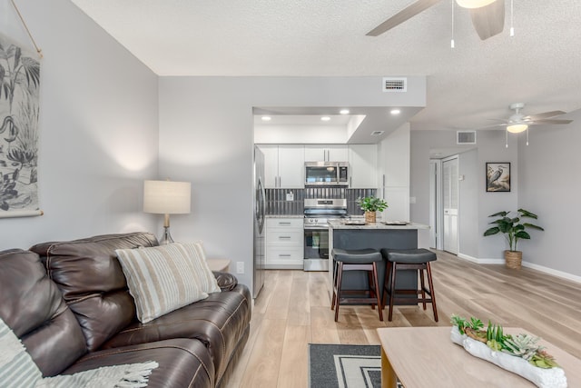 living room with a textured ceiling, light wood-type flooring, and ceiling fan