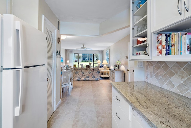 kitchen featuring tasteful backsplash, light stone counters, ceiling fan, white fridge, and white cabinetry