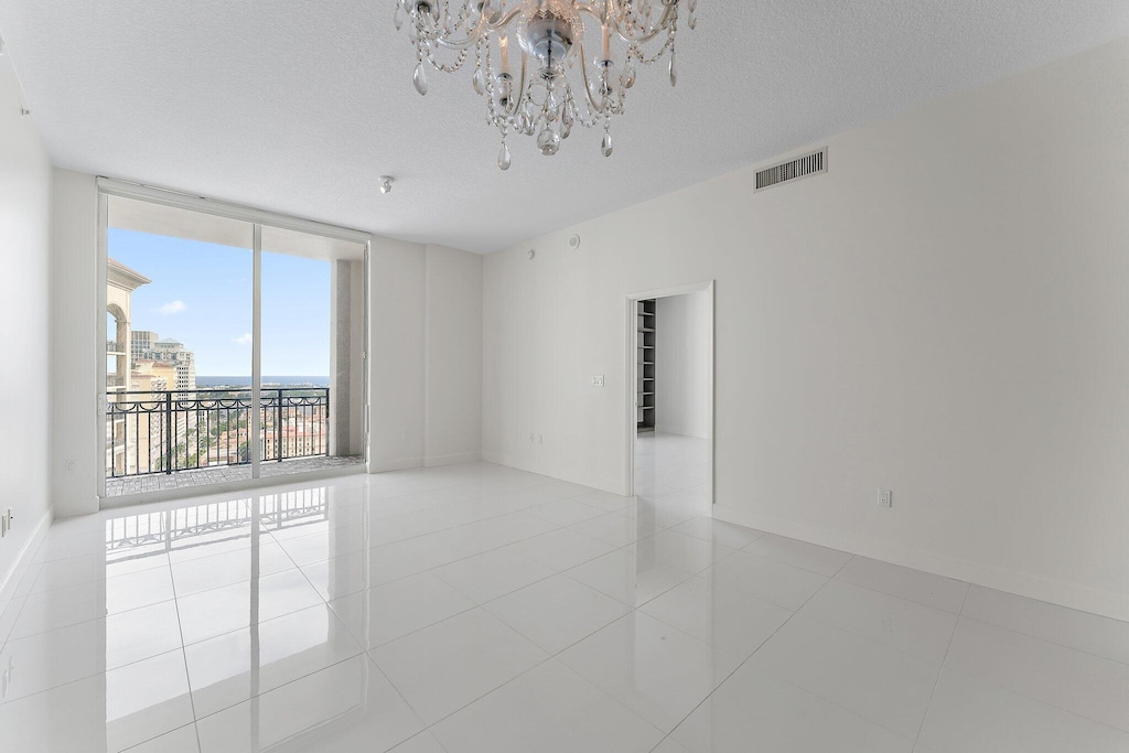 empty room with floor to ceiling windows, light tile patterned floors, a textured ceiling, and a chandelier