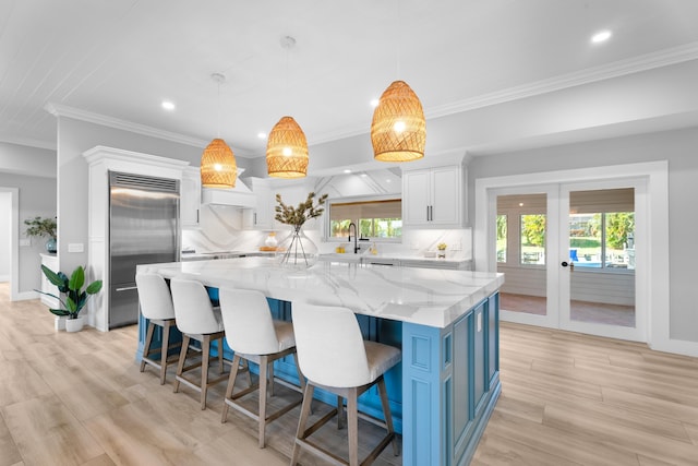 kitchen with white cabinetry, hanging light fixtures, stainless steel built in fridge, light stone countertops, and a spacious island