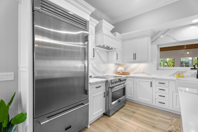 kitchen with stainless steel appliances, ornamental molding, custom range hood, and white cabinets