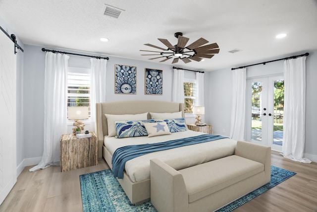 bedroom featuring multiple windows, a barn door, access to outside, and light hardwood / wood-style flooring