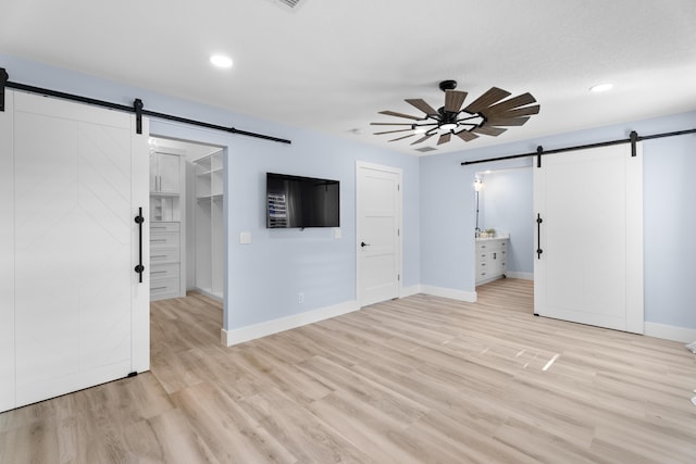 unfurnished bedroom with a walk in closet, a barn door, and light hardwood / wood-style flooring