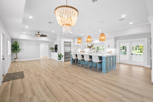 kitchen featuring pendant lighting, an island with sink, a breakfast bar area, white cabinets, and light hardwood / wood-style floors