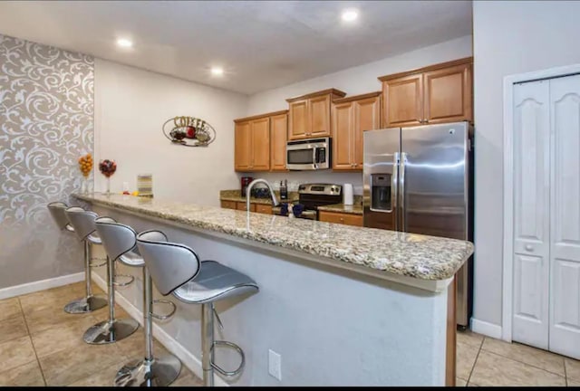 kitchen with light stone countertops, sink, kitchen peninsula, a breakfast bar, and appliances with stainless steel finishes