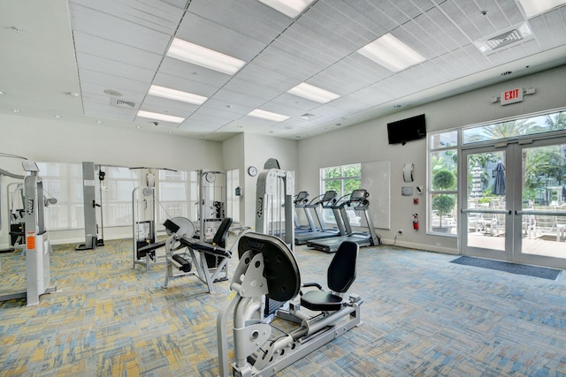 exercise room featuring a paneled ceiling, light carpet, french doors, and a towering ceiling