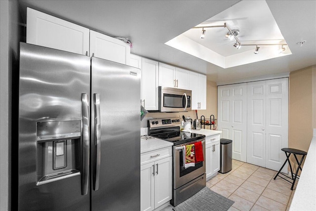 kitchen featuring appliances with stainless steel finishes, light tile patterned floors, a tray ceiling, and white cabinetry