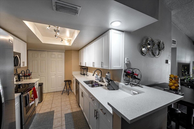 kitchen featuring a raised ceiling, sink, appliances with stainless steel finishes, light tile patterned flooring, and white cabinetry