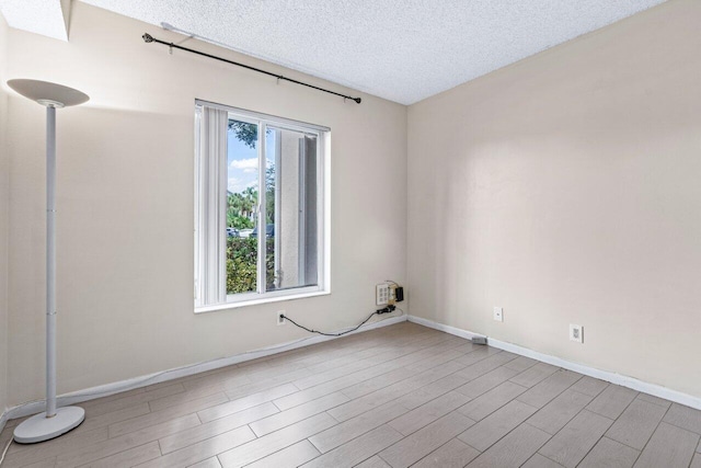 empty room with a textured ceiling and light hardwood / wood-style flooring