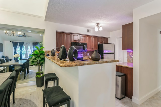 kitchen with ceiling fan with notable chandelier, range with electric cooktop, stainless steel fridge, kitchen peninsula, and a breakfast bar area