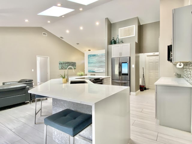 kitchen with a large island with sink, a kitchen breakfast bar, sink, a skylight, and stainless steel fridge