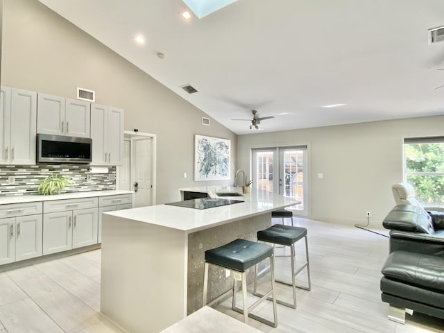 kitchen with ceiling fan, a wealth of natural light, a breakfast bar area, and an island with sink