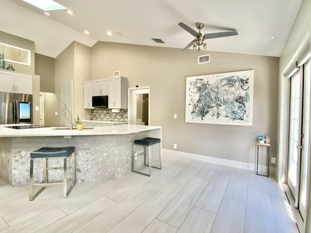 kitchen featuring white cabinetry, stainless steel fridge, a breakfast bar area, and vaulted ceiling