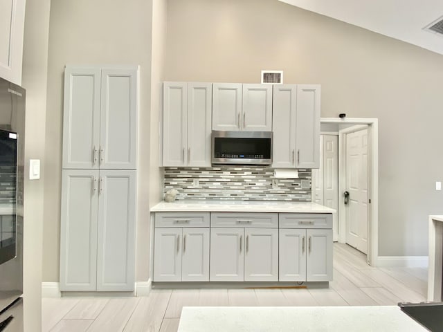 kitchen featuring tasteful backsplash, high vaulted ceiling, and light wood-type flooring