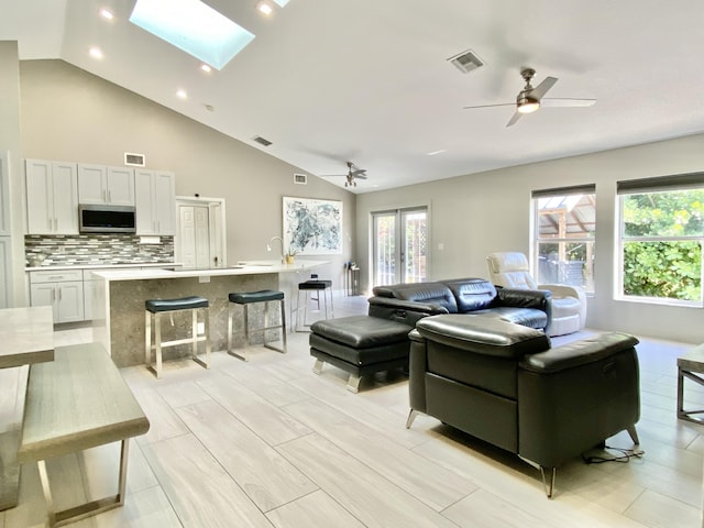 living room with ceiling fan, high vaulted ceiling, and a skylight