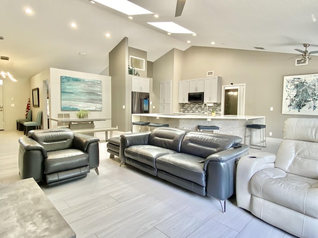 living room with light wood-type flooring, a skylight, ceiling fan, sink, and high vaulted ceiling