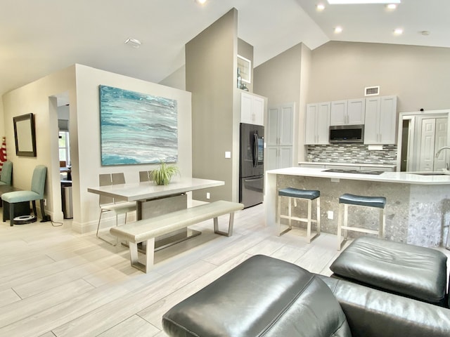 living room featuring sink, high vaulted ceiling, and light hardwood / wood-style floors