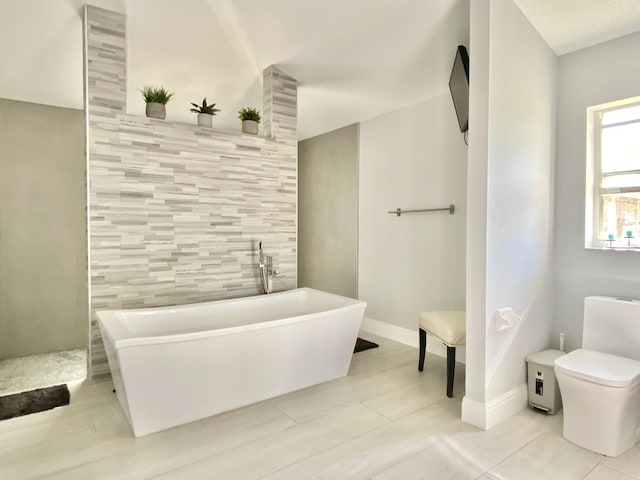 bathroom with tile patterned flooring, a tub to relax in, toilet, and tile walls