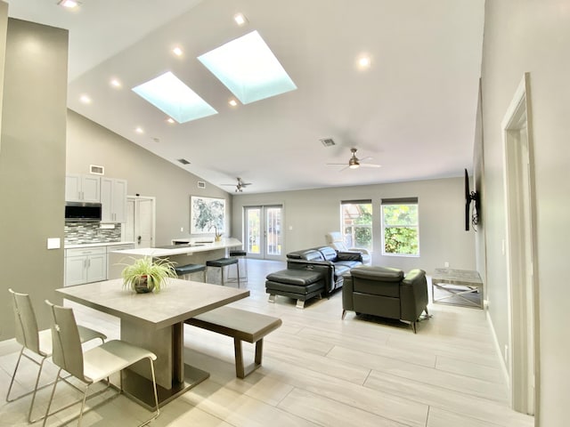 dining room with light wood-type flooring, a skylight, high vaulted ceiling, and ceiling fan