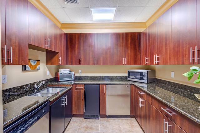 kitchen with a paneled ceiling, dark stone countertops, sink, and appliances with stainless steel finishes