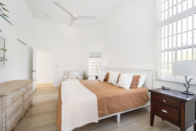 bedroom with ceiling fan, a high ceiling, and light hardwood / wood-style flooring