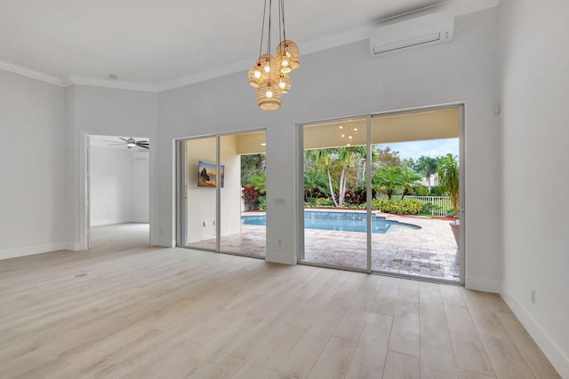 spare room featuring a wall mounted air conditioner, ceiling fan with notable chandelier, ornamental molding, a towering ceiling, and light hardwood / wood-style floors