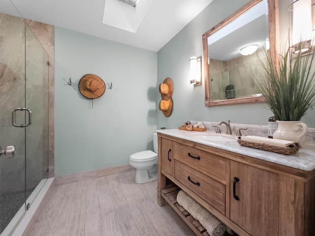 bathroom featuring vanity, toilet, a shower with shower door, and a skylight