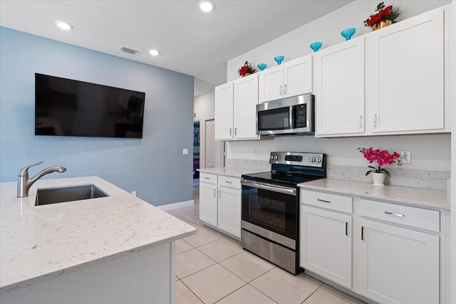 kitchen with light stone countertops, sink, stainless steel appliances, light tile patterned floors, and white cabinets