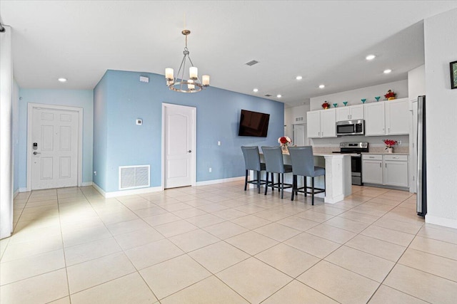 kitchen featuring appliances with stainless steel finishes, a breakfast bar, decorative light fixtures, white cabinets, and a center island