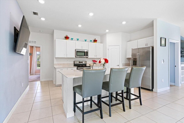 kitchen featuring a kitchen bar, white cabinetry, stainless steel appliances, and a kitchen island with sink