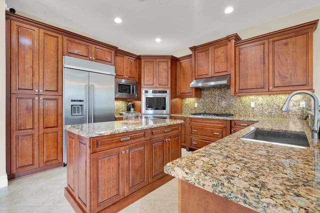 kitchen featuring backsplash, light stone counters, sink, built in appliances, and a center island