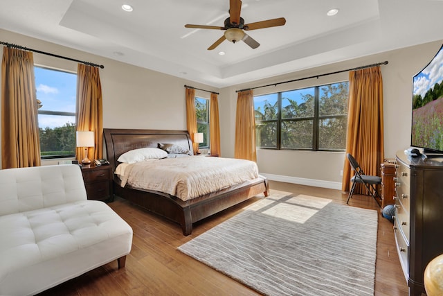 bedroom featuring a tray ceiling, multiple windows, ceiling fan, and hardwood / wood-style floors