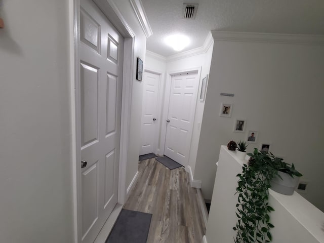 hall featuring light wood-type flooring, a textured ceiling, and ornamental molding