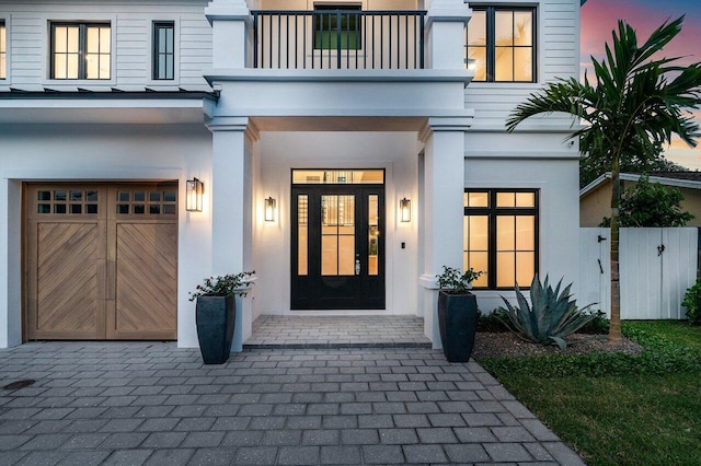 exterior entry at dusk featuring a balcony and a garage