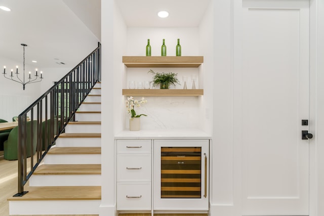 bar with hanging light fixtures, an inviting chandelier, tasteful backsplash, wine cooler, and wood-type flooring