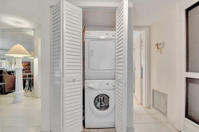 clothes washing area featuring light tile patterned floors, a textured ceiling, and stacked washer and clothes dryer