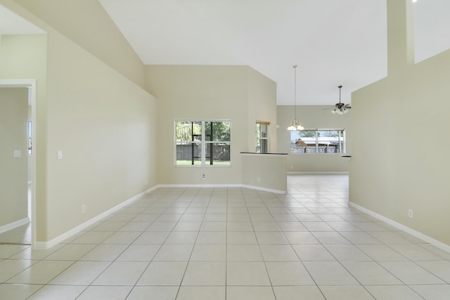 unfurnished living room with ceiling fan with notable chandelier, a healthy amount of sunlight, light tile patterned flooring, and high vaulted ceiling