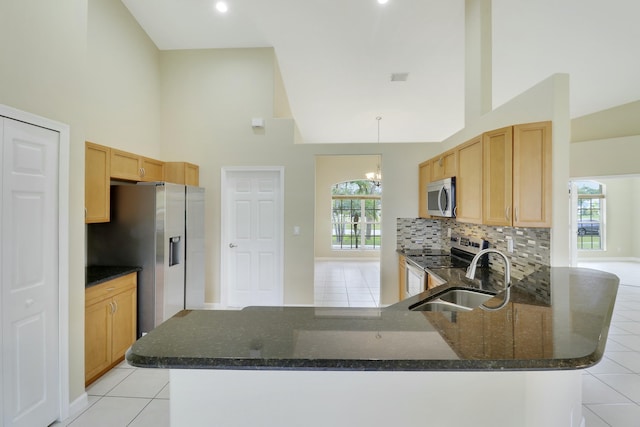 kitchen featuring kitchen peninsula, a high ceiling, stainless steel appliances, and dark stone counters