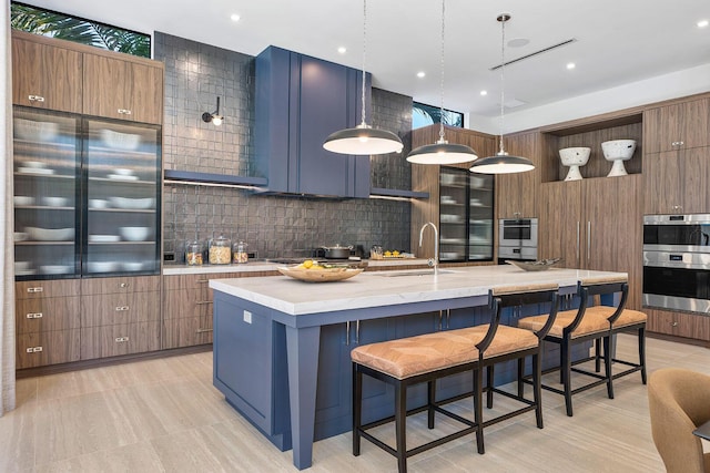 kitchen featuring a center island with sink, sink, decorative backsplash, decorative light fixtures, and a breakfast bar area