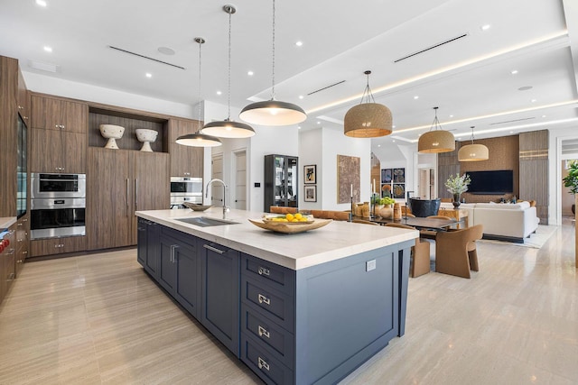 kitchen featuring double oven, decorative light fixtures, sink, and a large island with sink