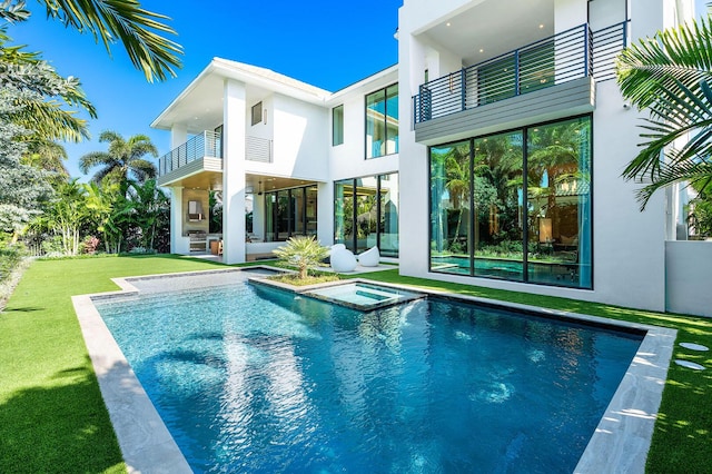 rear view of house with a pool with hot tub, a balcony, and a yard