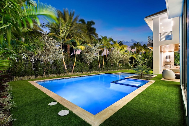 pool at dusk featuring a lawn and an in ground hot tub