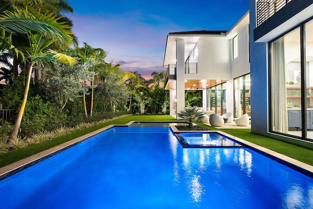 pool at dusk with an in ground hot tub