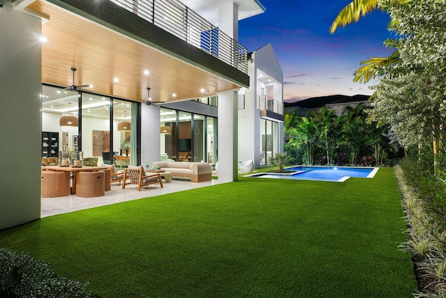 back house at dusk with a lawn, a patio area, an outdoor living space, and a balcony