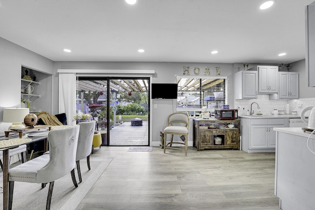 kitchen with white cabinets, light wood-type flooring, backsplash, and sink