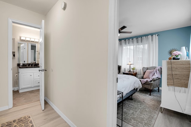 bedroom featuring sink, light wood-type flooring, ceiling fan, and connected bathroom